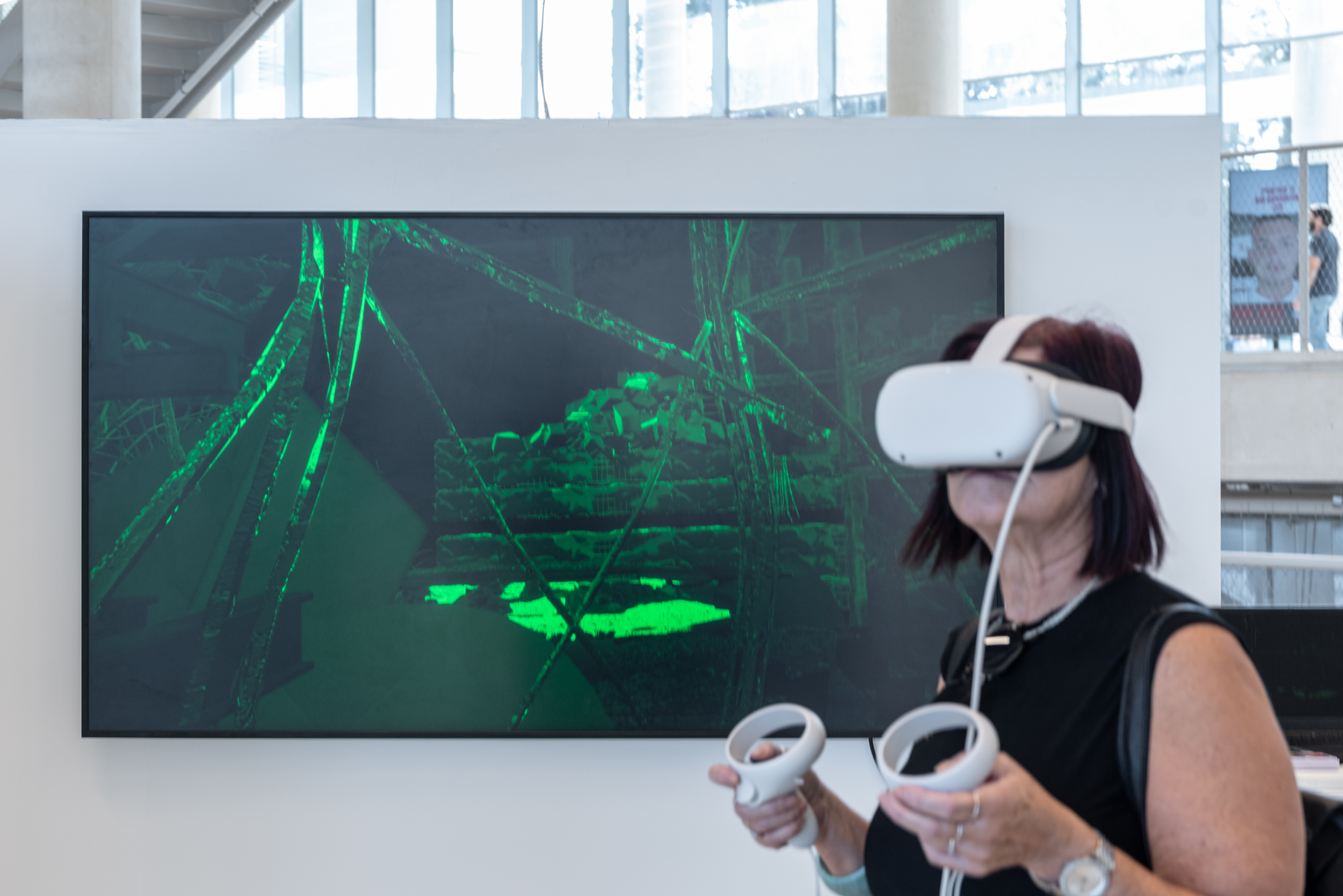 Visitor in VR headset — holding controllers, green ruin scene visible behind